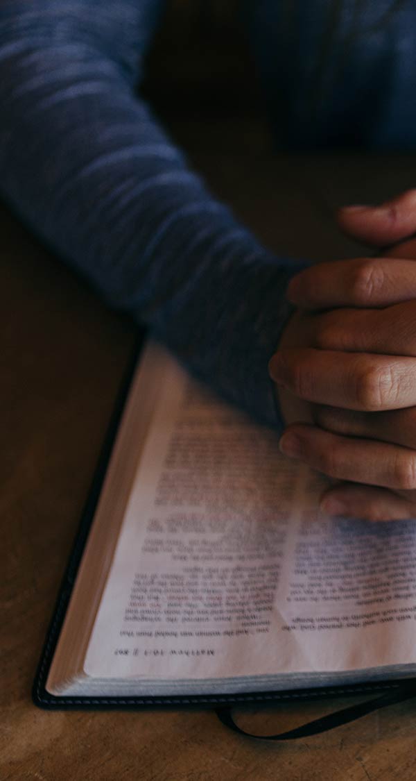 Man with prayer hands and a bible at a table