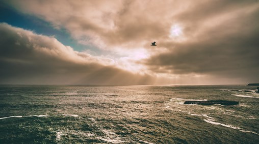 A picture of the ocean with a beautiful cloudy sky with the sun breaking through