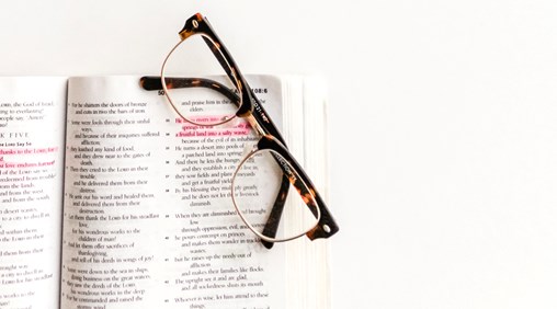 A picture of a bible with a reading glasses placed at the top