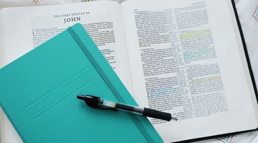 A bible with a coloured notepad and pen on top of it